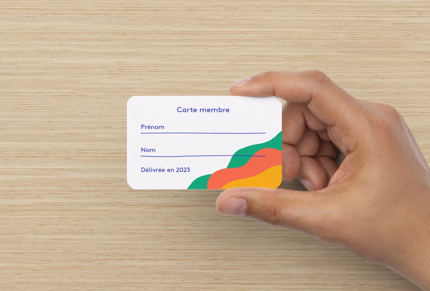 Maquette d'une carte membre tenue en main : « Carte membre », champs Prénom et Nom, « Délivrée en 2023 », vagues vertes, orange et jaunes dans le coin.