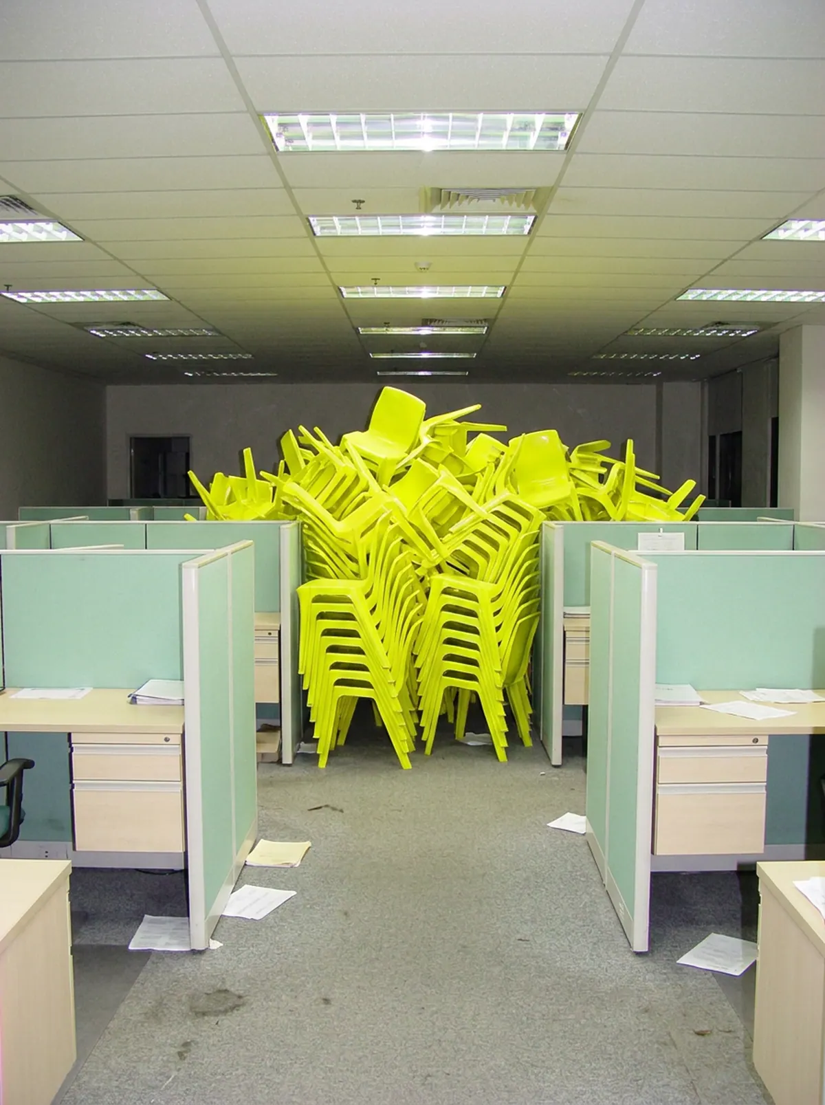 Open space déserté : des chaises jaune fluo s'empilent en tas au milieu des cloisons de bureau.