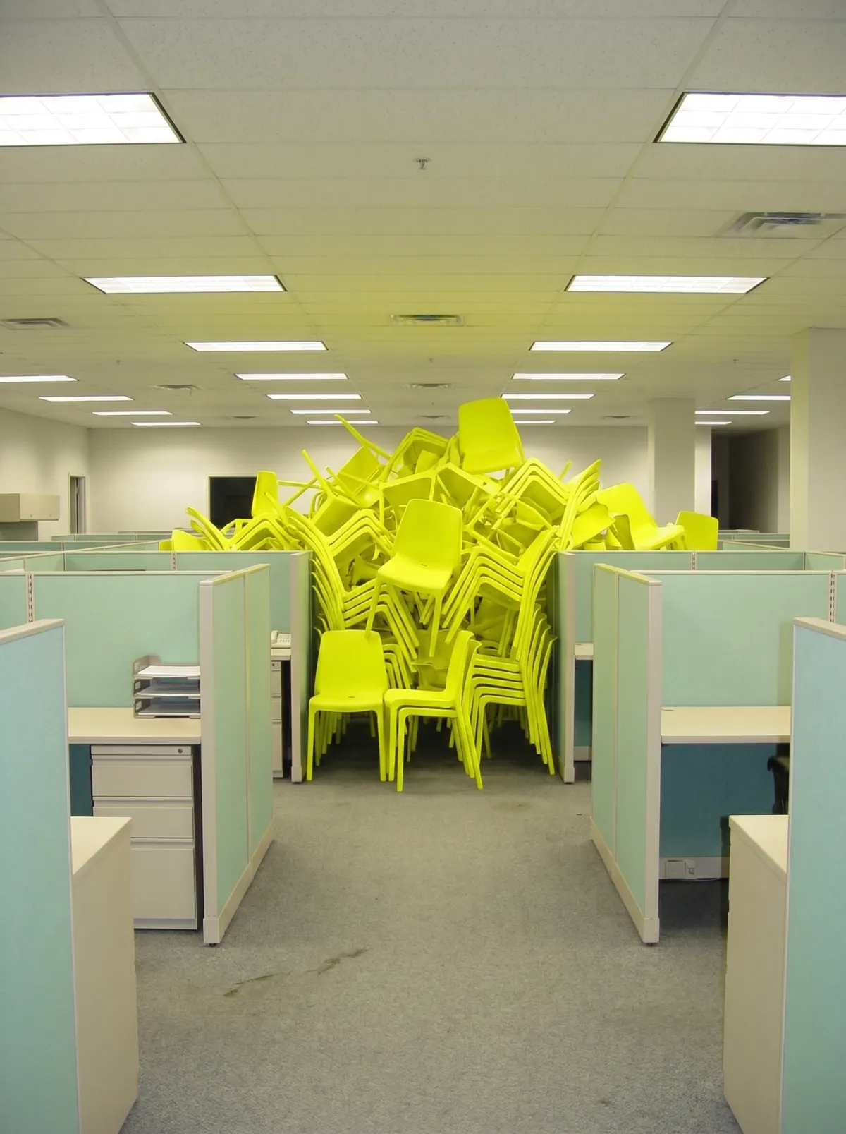 Rangée de box de bureau où s'empilent des chaises jaune fluo